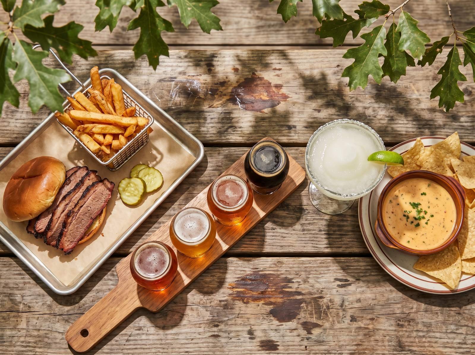 Brisket sandwich, fries, a flight of four beers, a frozen margarita and queso on a picnic table